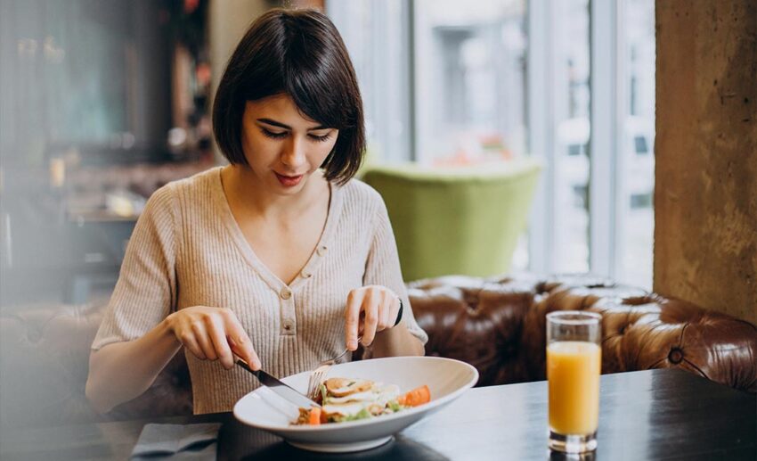 A young woman enjoying a quiet morning breakfast with fresh juice at a local cafe, representing simple, anchoring daily routines while travelling.