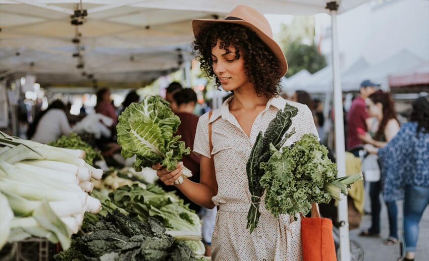 A woman selecting fresh lettuce heads while shopping at a local outdoor produce market