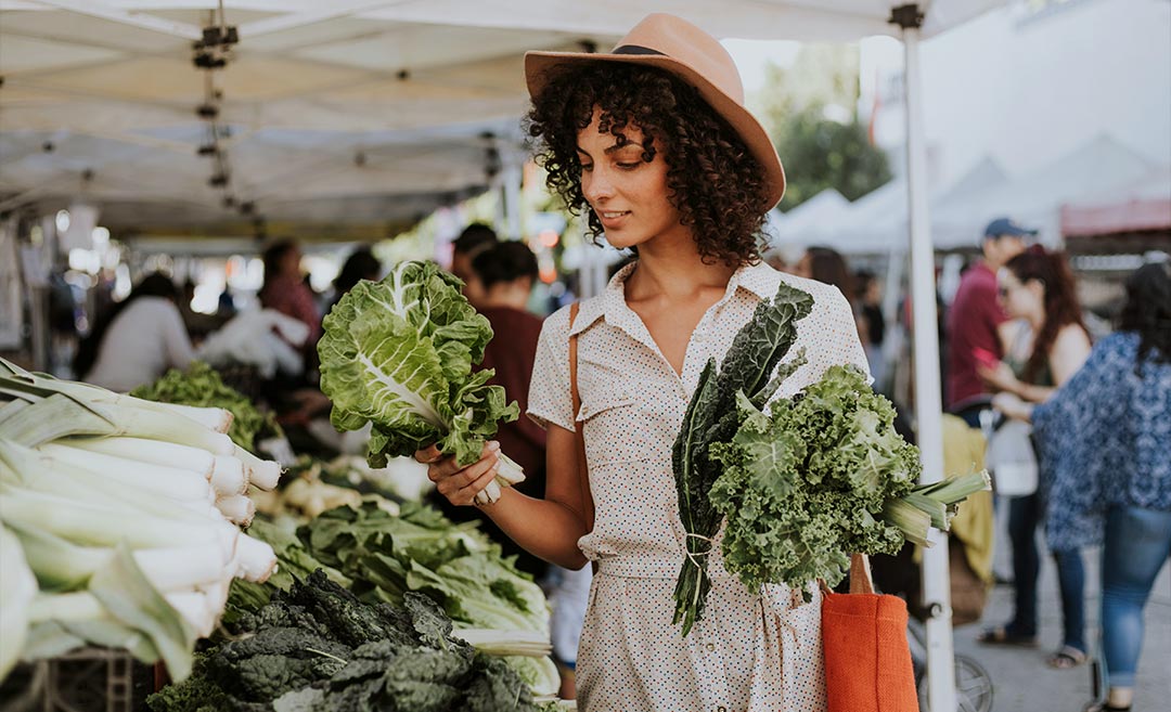 A woman selecting fresh lettuce heads while shopping at a local outdoor produce market