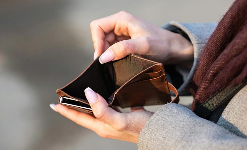 A close-up view of a person's hands holding an open, empty leather wallet alongside a smartphone, illustrating the financial uncertainty and income fluctuations of freelance travel work.