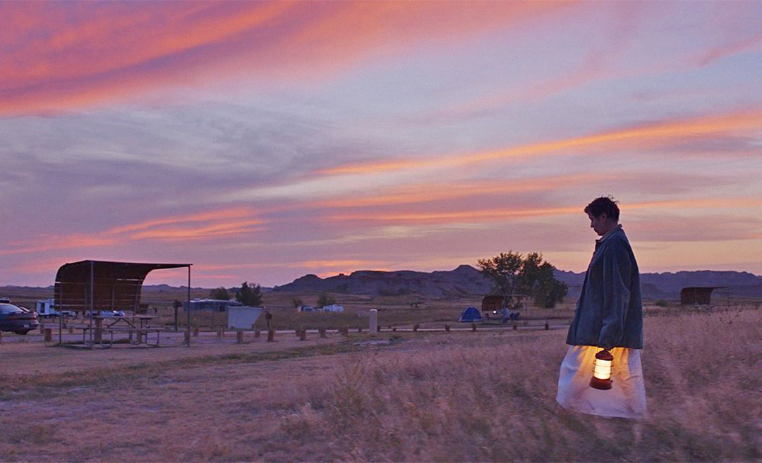 A screengrab from the movie, Nomadland, directed by Chloe Zhao, featuring actress Frances McDormand walking across a vast plain at dusk.