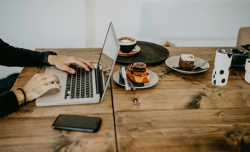 digital nomad typing on a laptop computer placed on a rustic wooden table, representing location-independent remote work.