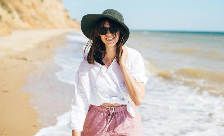 A woman walking along the shoreline in gentle tropical sea waves under a clear blue sky, illustrating the hope of rediscovering joy and warmth through travel.
