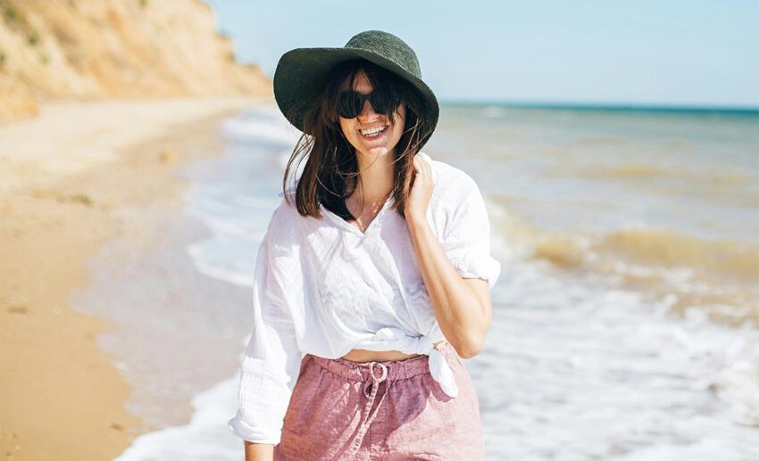 A woman walking along the shoreline in gentle tropical sea waves under a clear blue sky, illustrating the hope of rediscovering joy and warmth through travel.