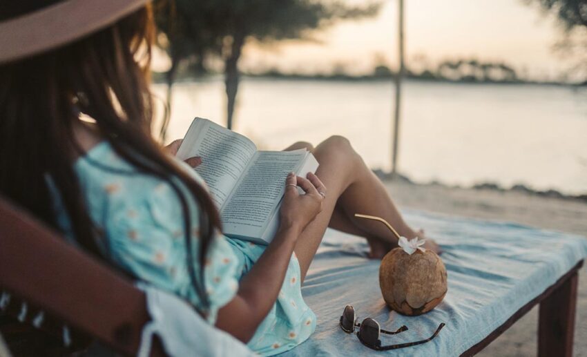 A woman relaxing on a Zanzibar beach at sunset, reading a book with a fresh coconut drink nearby while maintaining a remote work-life balance.