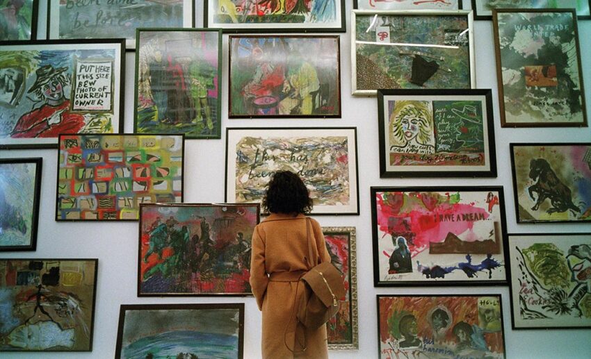 Woman standing in reflection before an art gallery exhibition wall covered in framed pictures in Turkey.