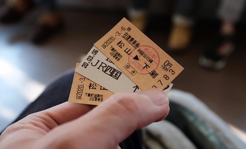 Person holding brown and black train ticket stubs at Shimonada Station in Japan