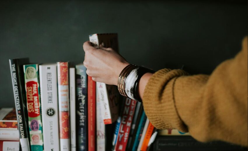 Close-up of a woman's hand selecting a book from a wooden bookshelf at Native Hostel in Austin, United States