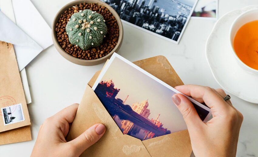 Close-up of a woman's hands pulling handwritten travel postcards out of a brown envelope.