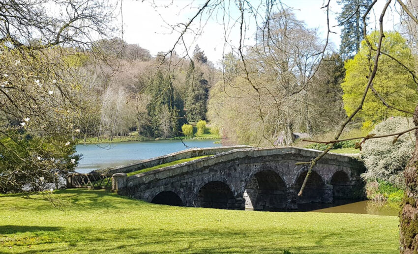 Scenic view of Stourhead Gardens in Wiltshire, featuring the classical Temple of Apollo surrounded by lush trees and a lake