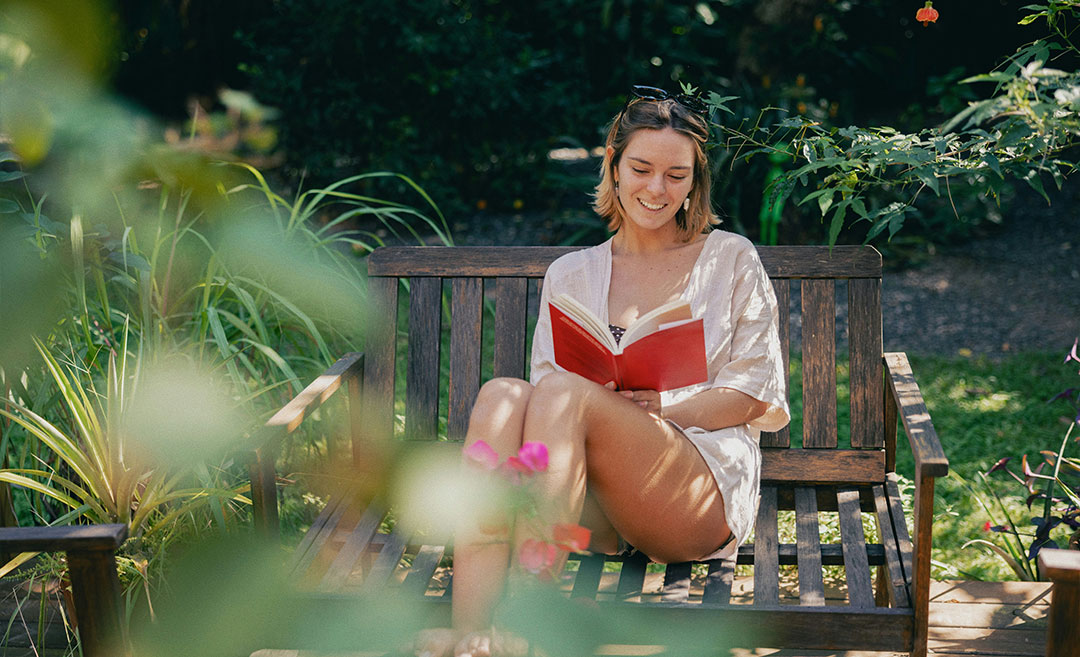 Smiling woman sitting on a wooden garden bench outdoors while reading a book
