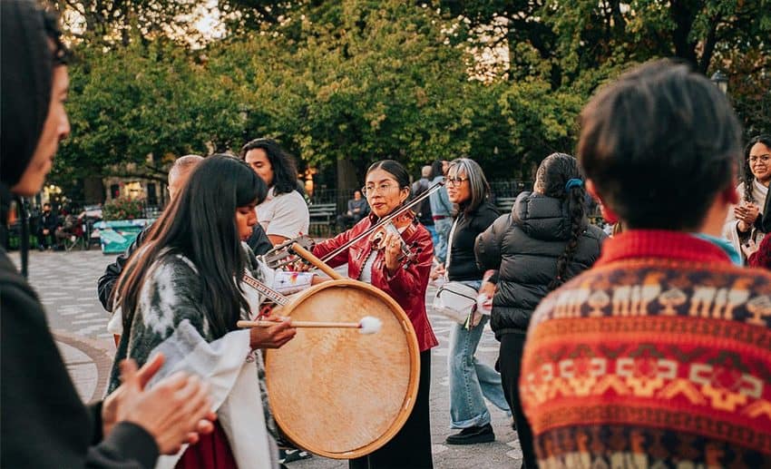 A diverse group of musicians playing acoustic instruments outdoors during an informal community gathering.
