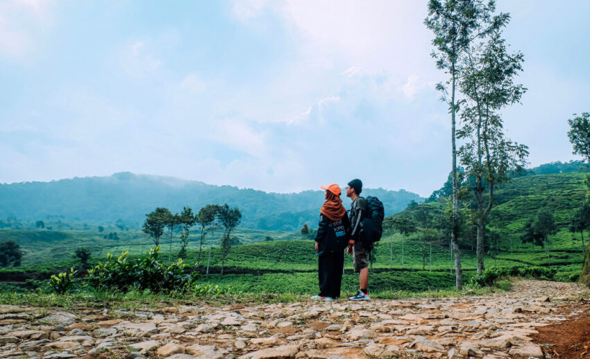 Malaysian couple standing on a mountain dirt road on vacation, taking in scenic countryside views while exploring outdoors.