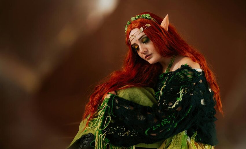 Woman wearing a detailed green historical cosplay dress with red hair at an outdoor live-action roleplay event.