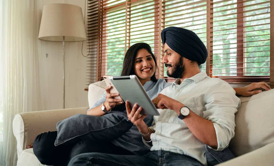 Couple relaxing on a living room sofa while browsing travel itineraries on a tablet computer at home.