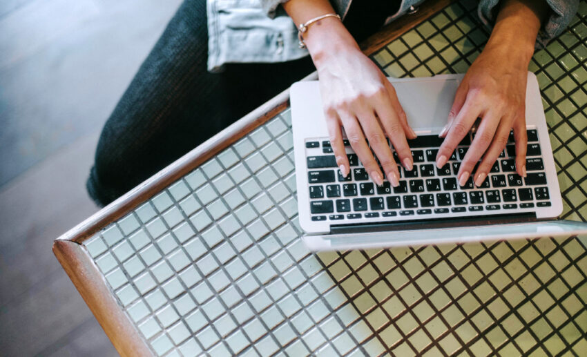Overhead shot of a woman typing on a laptop over a checkered tablecloth while reviewing travel plans and insurance details.