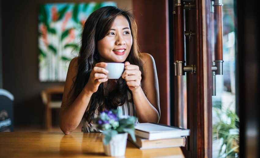 A smiling woman relaxing with a cup of coffee inside a brightly lit local café during a travel stop.