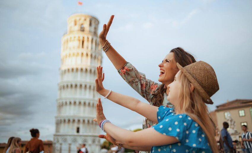 Two women posing creatively to hold up the Leaning Tower of Pisa in Italy during a travel trip.