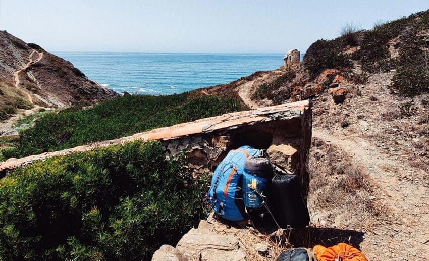 Hiking trail leading towards the Atlantic Ocean along Portugal’s Alentejo coast, with backpacks beside the path.