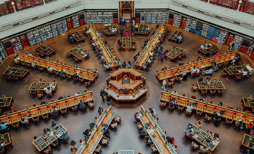 High-angle view of students studying at desks in a grand, historic library reading room in Melbourne, Australia.