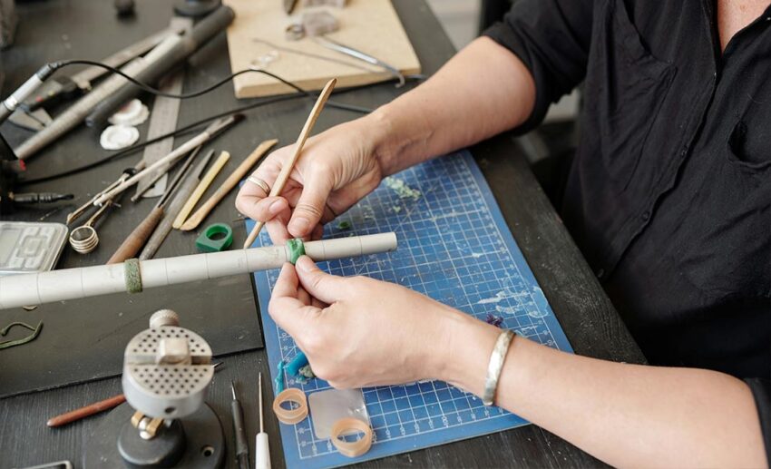 Close-up of a jeweller’s hands working at a workbench with tools, sizing a metal ring during a hands-on craft workshop.