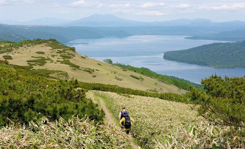 Hikers traversing volcanic terrain and wetlands along the East Hokkaido Trek in wilderness Japan.