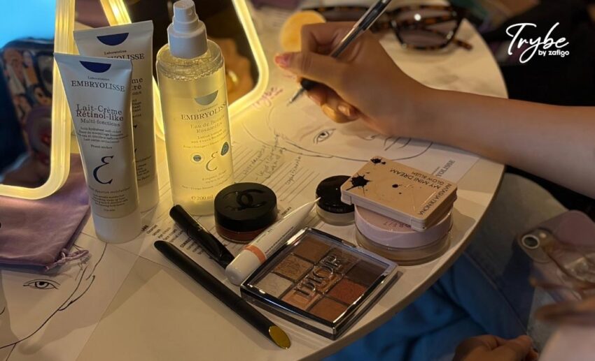 Close-up of a participant's table with an illuminated vanity mirror, beauty products, and a hand writing notes on a masterclass worksheet.