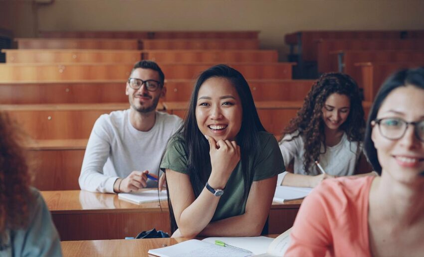 Smiling adult students sitting in a bright university lecture hall classroom during an immersive group learning session.