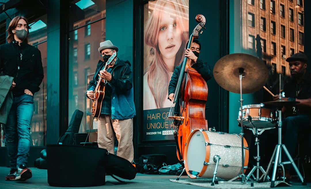 Street violin player and a live outdoor jazz band performing for passers-by on a street in New York City.