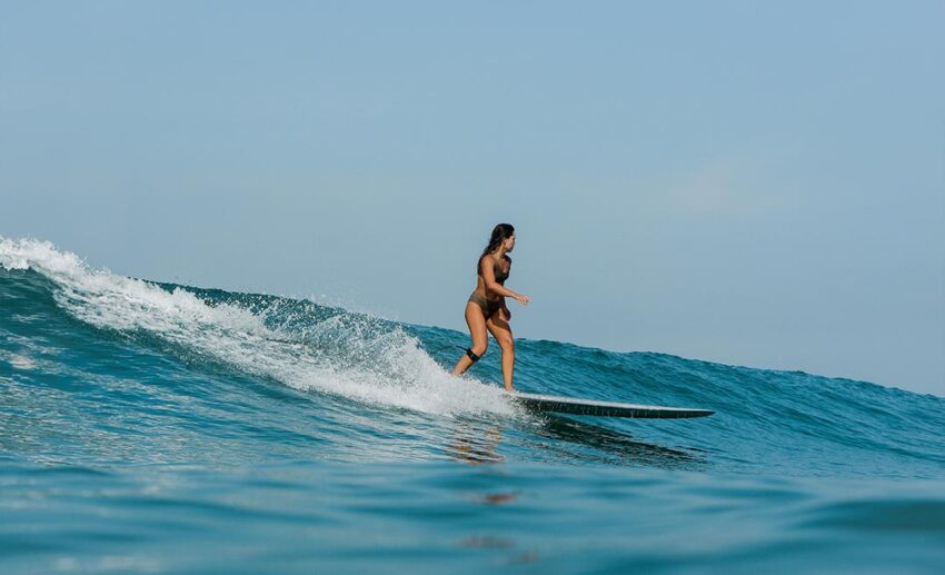 Female surfer balancing and riding a breaking wave in the ocean on a surfboard.
