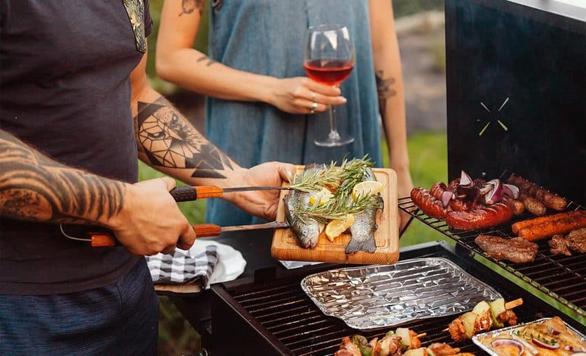 A man and a woman cooking food together on an outdoor grill during a getaway.