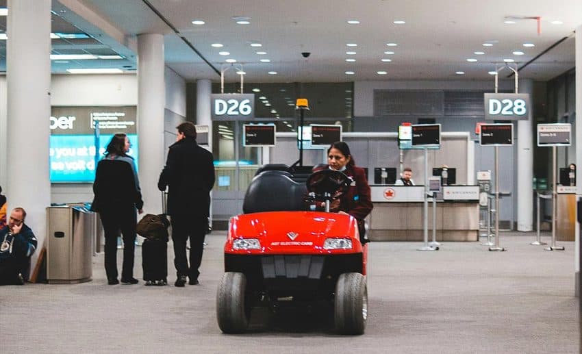 A female airport assistant driving a passenger buggy through a bright airport terminal.