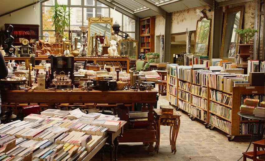 A cosy independent vintage bookshop in Paris filled with stacks of second-hand books, antique furniture, and floor-to-ceiling shelves.