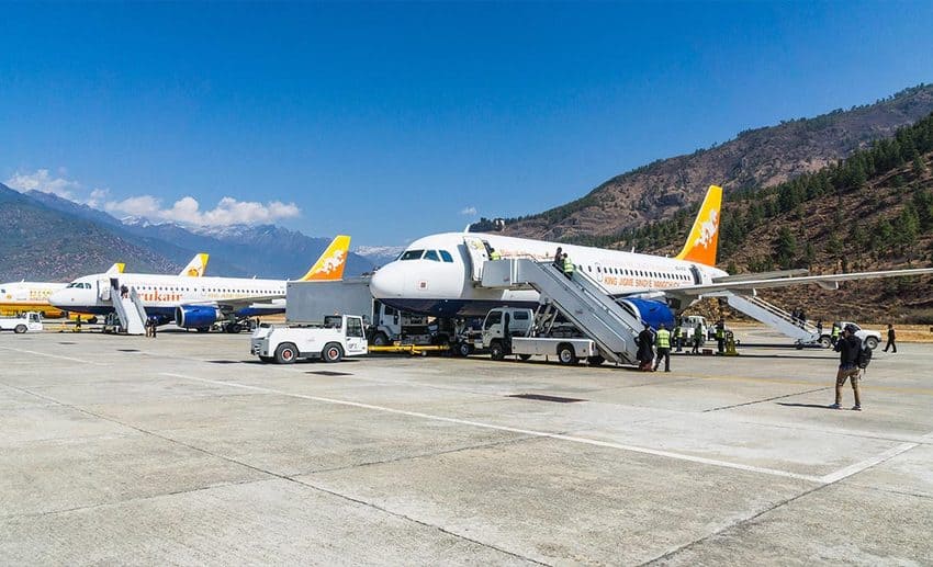 Passengers walking across the tarmac after arriving at Paro International Airport, framed by dramatic Himalayan mountain peaks in Bhutan.