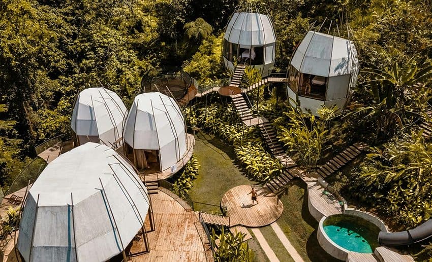 A bird's-eye drone view of a luxury tropical villa and secluded canvas tents tucked away amidst lush green Costa Rican rainforest canopy.