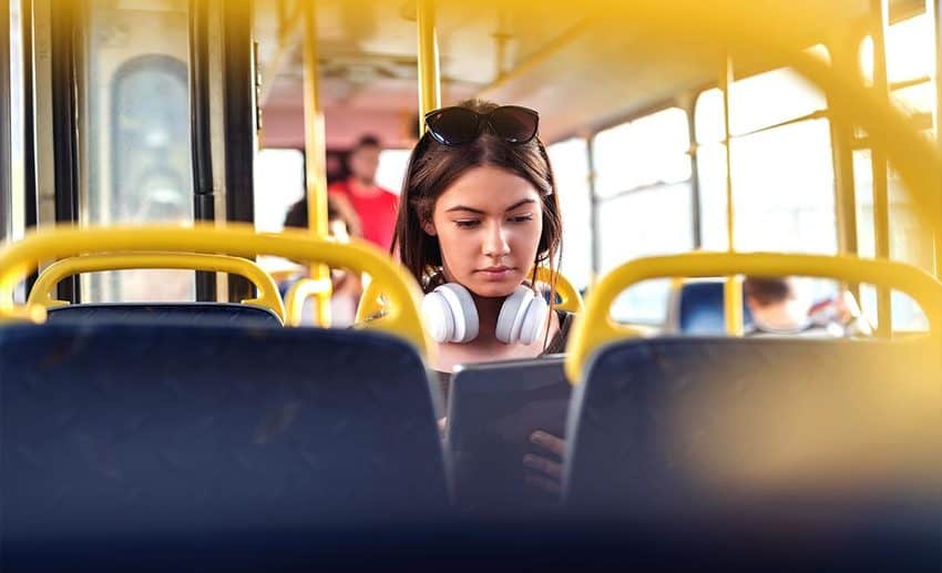 A traveller wearing headphones sitting on public transport while watching a tablet.