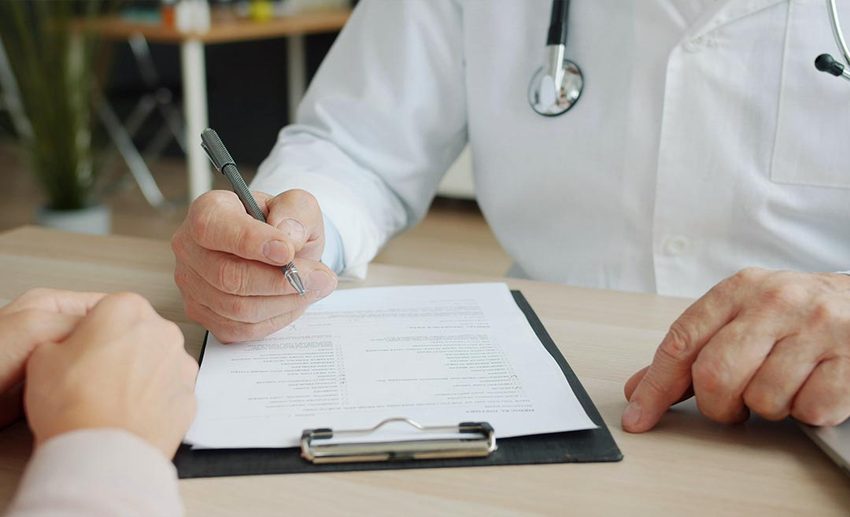 A doctor writing medical notes and generic prescription details on a patient's chart during a pre-travel consultation.