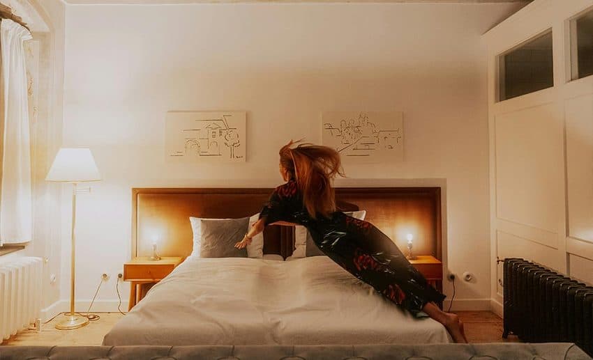A woman in pyjamas jumping onto a comfortable hotel bed during a holiday.
