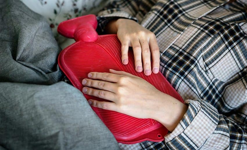Close-up of a woman pressing a warm water heat pack against her lower stomach for menstrual cramp relief.