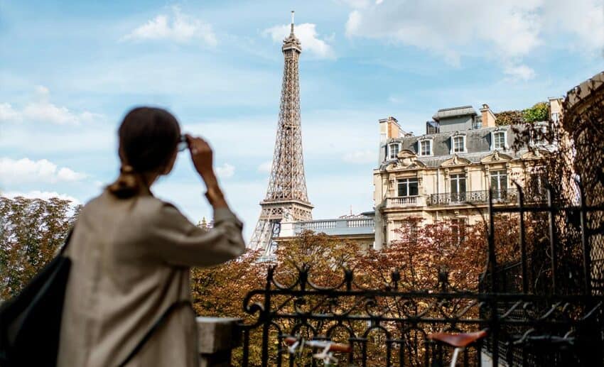 A woman gazing out at the Eiffel Tower in Paris, with the iconic landmark softly focused in the background.